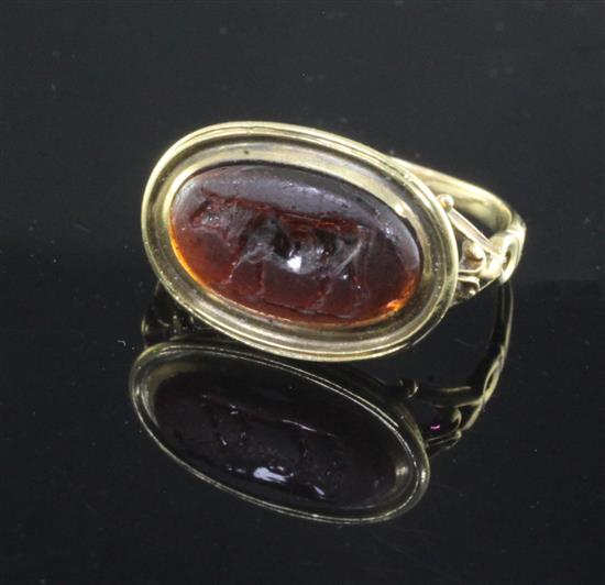 An antique yellow metal and oval carnelian cabochon ring carved with a standing bull, the shank with decorative pierced shoulders